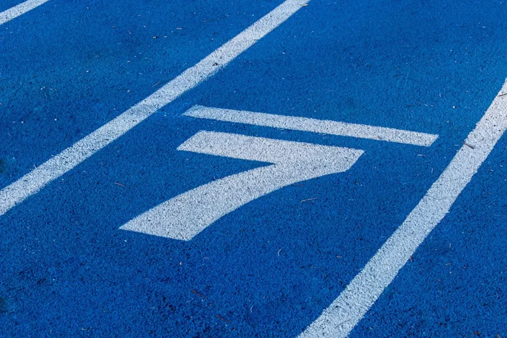 Une piste d'athlétisme bleue, avec des lignes de couloir blanches, arbore un grand chiffre sept peint. La texture et la couleur dégagent une atmosphère dynamique et pleine d'énergie.