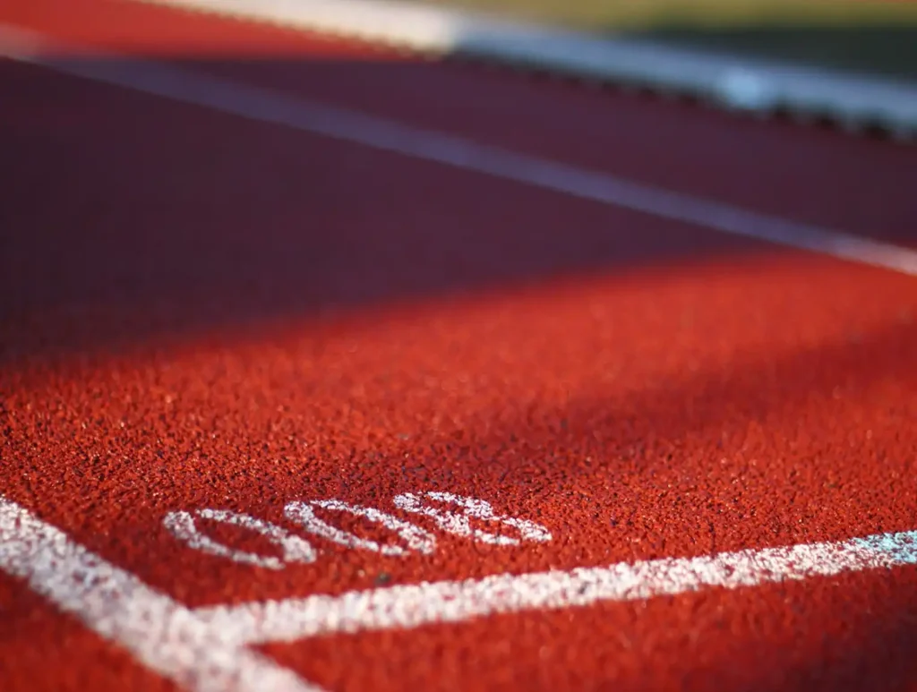 Gros plan sur une piste d'athlétisme rouge marquée du chiffre « 800 » en blanc, mettant en valeur la surface texturée et les lignes de démarcation nettes sous la douce lumière du soleil.