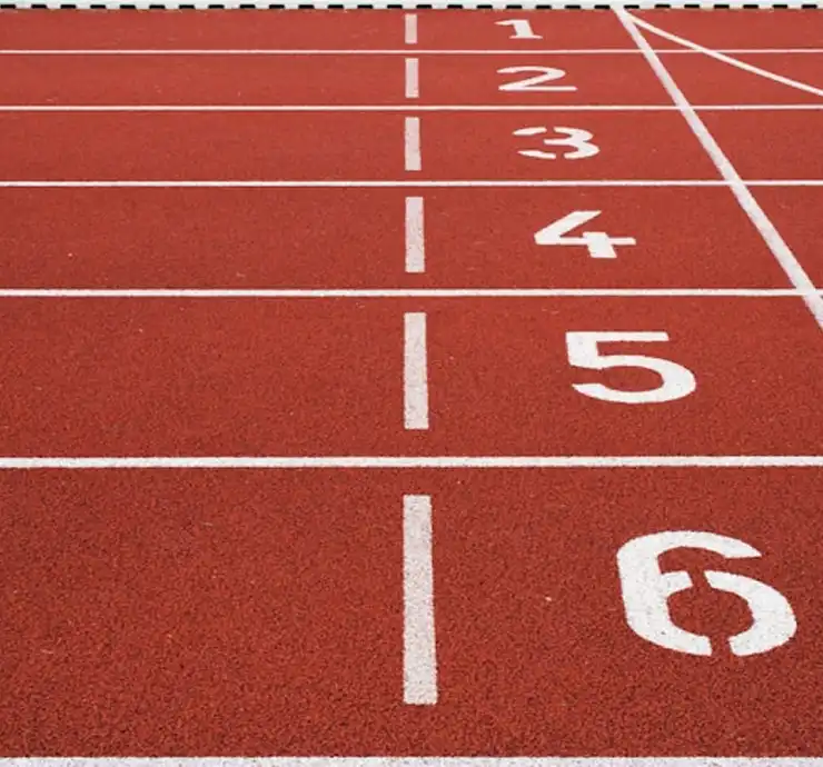 Une piste d'athlétisme rouge comportant six couloirs numérotés de 1 à 6 en blanc. La vue est orientée vers la ligne d'arrivée, ce qui suggère un sentiment de préparation et d'anticipation.