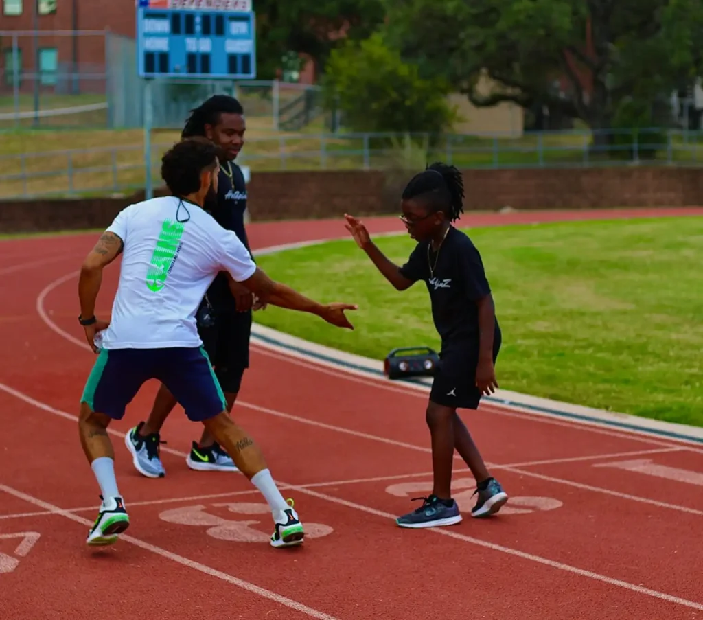 Trois personnes sur une piste célèbrent une course réussie. Un homme tape dans la main d'un garçon souriant, dans un élan de solidarité et d'encouragement. Un tableau d'affichage est visible à l'arrière-plan.