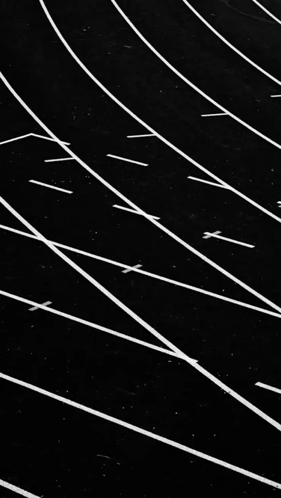 Image en noir et blanc représentant des lignes courbes sur une surface sombre, évoquant une piste d'athlétisme. Ces lignes forment un motif abstrait et dynamique qui suggère le mouvement.