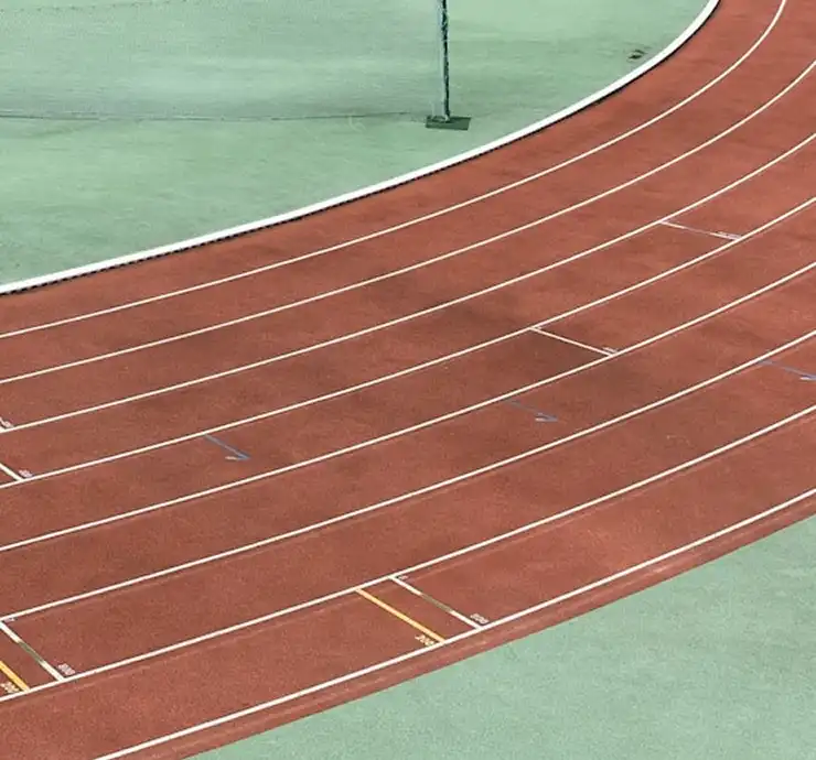 Une section incurvée d'une piste d'athlétisme vide, avec des couloirs d'un rouge vif et des lignes blanches, se détachant sur un fond vert contrastant, qui dégage une atmosphère sereine et bien organisée.