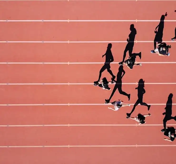 Vue aérienne de plusieurs coureurs sur une piste rouge, projetant des ombres allongées. L'image rend compte du mouvement dynamique et de l'énergie d'une course en cours.